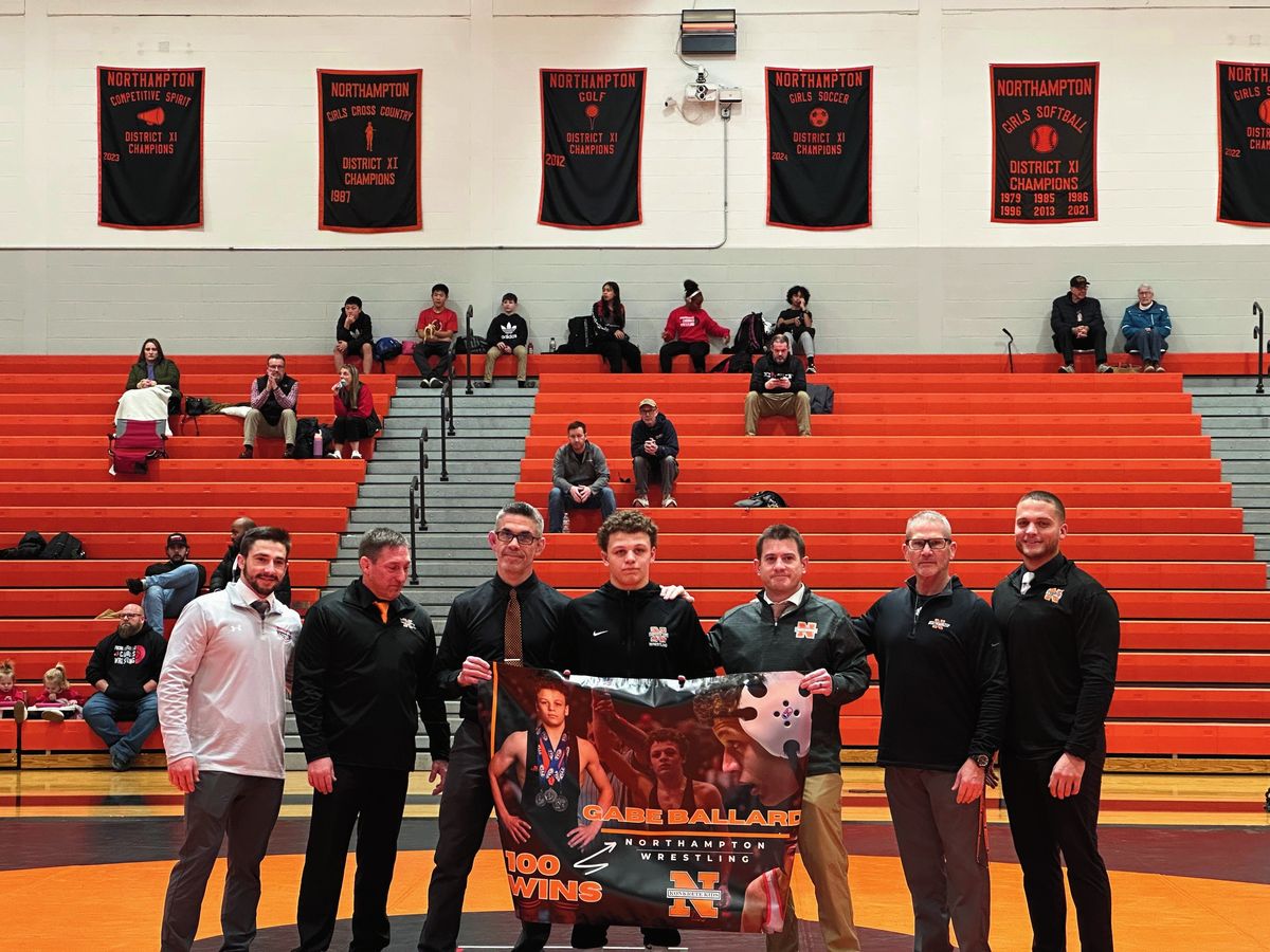 Gabe Ballard holds a banner marking his 100th career win, flanked by his coaches