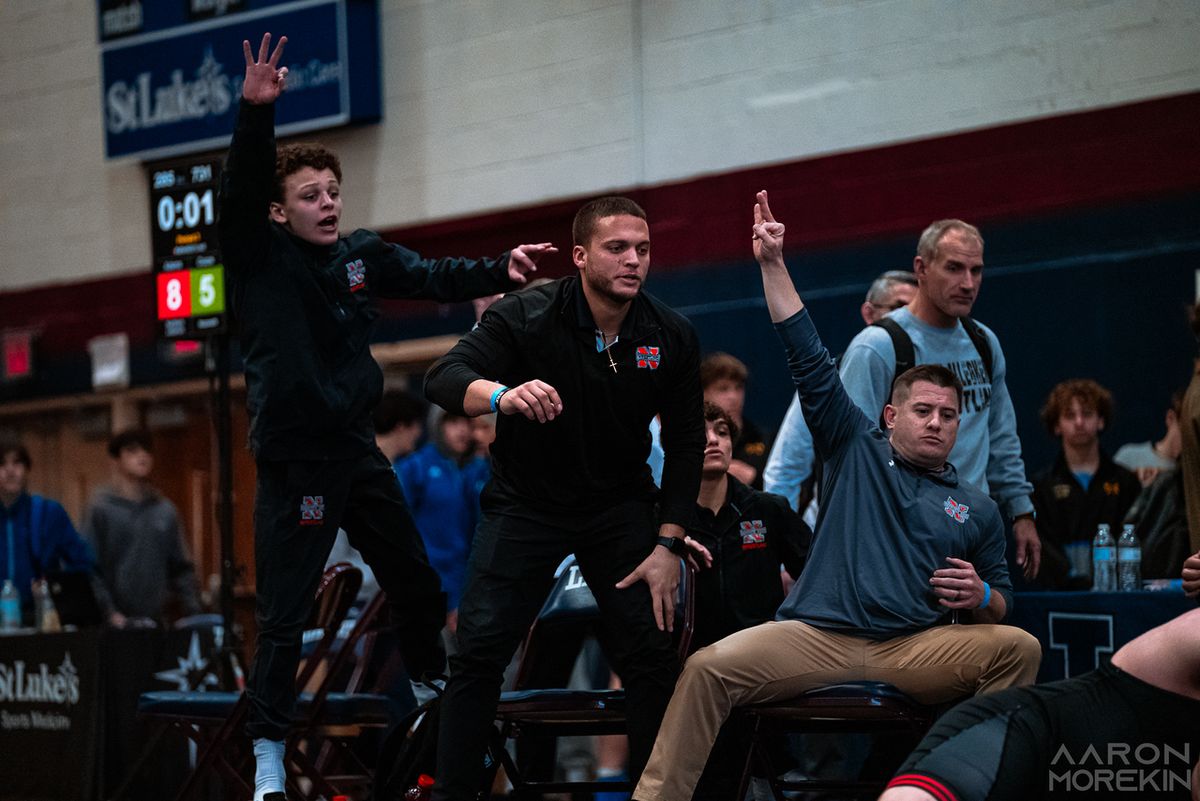 Northampton coaches and wrestlers rise from the bench and signal with the clock at one second
