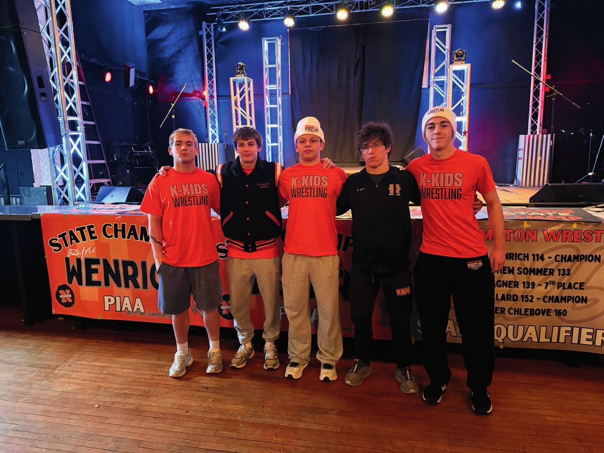 Wrestlers in K-Kids shirts pose in front of a State Champion Wenrich banner