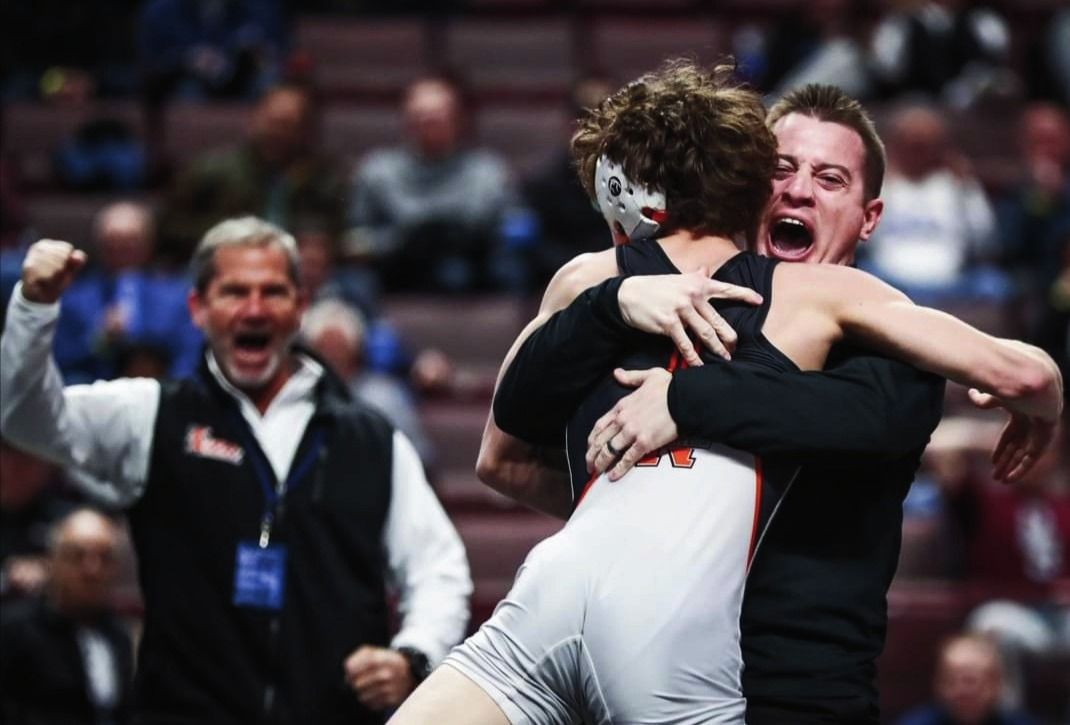 Coach Joe Provini lifts Carson Wagner in a hug as another coach cheers behind them