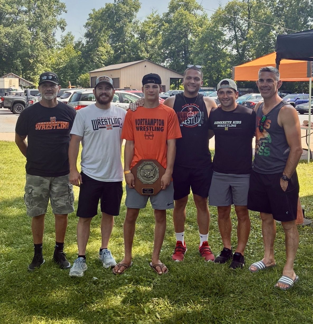 Brayden Wenrich holds his Fargo plaque, standing on the grass with five Northampton coaches