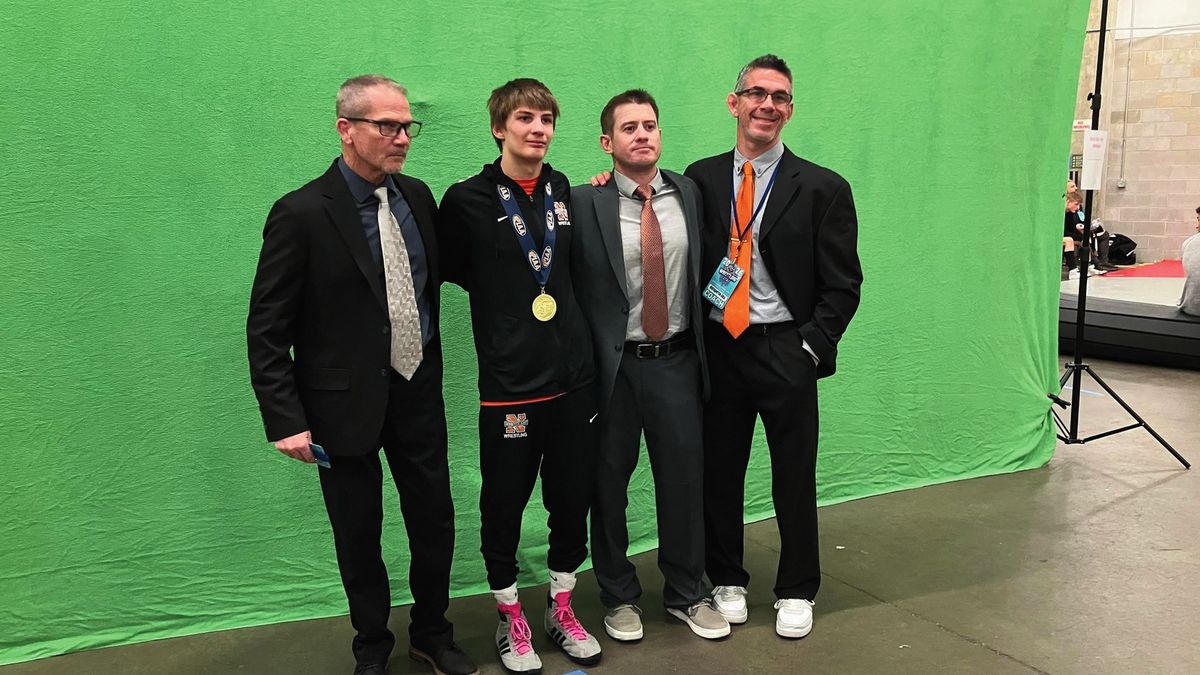 Brayden Wenrich, wearing a gold medal, stands with three men in suits in front of a green screen