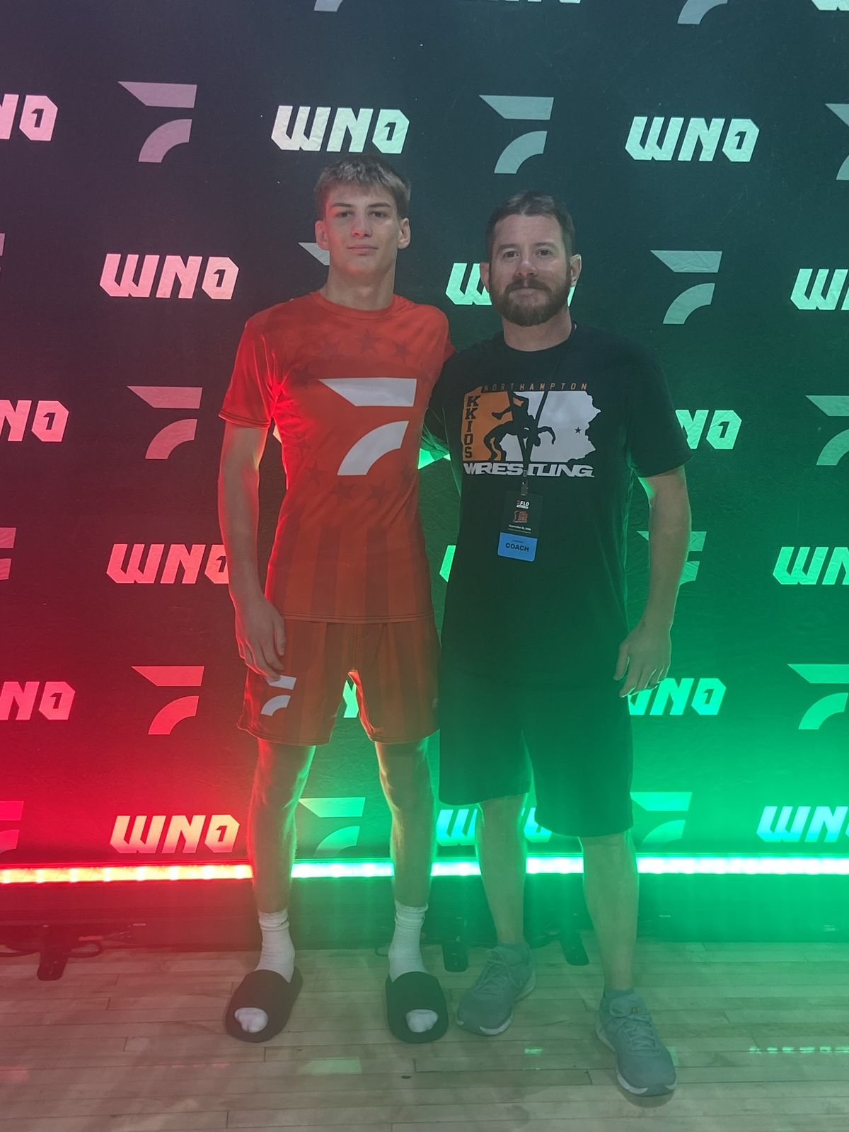 Brayden Wenrich stands with a Northampton coach in front of the lit Who's Number One backdrop