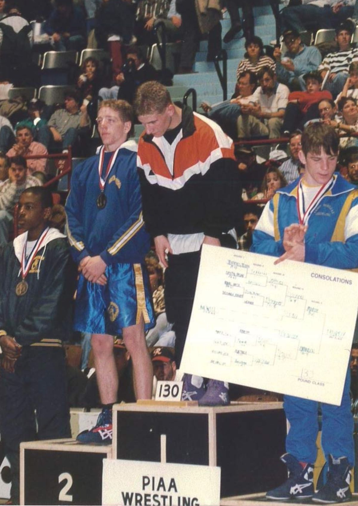 Whitey Chlebove stands on the top step of the PIAA podium at 130 pounds in a Northampton warm-up jacket, beside the other medalists