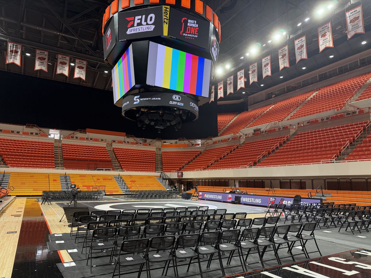 Gallagher-Iba Arena set up for Who's Number One, with orange seats, the center scoreboard and the mat surrounded by chairs